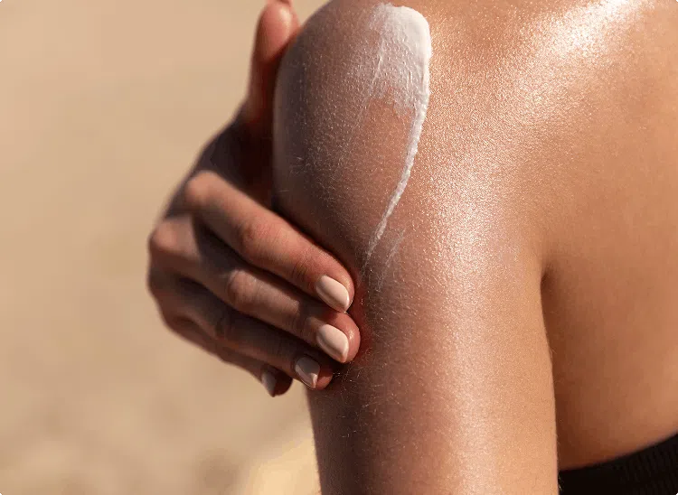 Person applying sunscreen to their shoulder, emphasizing sun protection on a beach or sunny day.