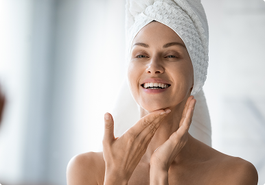 Improve Texture and Tone Smiling woman with a towel on her head touching her face, suggesting a fresh skincare or self-care routine.