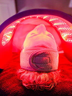 Red Light Therapy to rejuvenate your skin Person lying under red LED light panel with towel headband, highlighting facial red light therapy treatment.