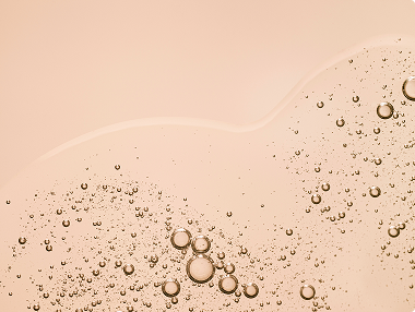 Close-up of clear serum or oil with bubbles on a peach background, suggesting a skincare product texture.