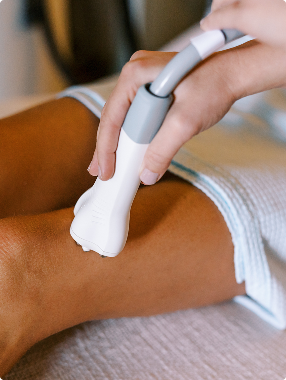 Close-up of a handheld device being used on a person's leg, suggesting a spa or cosmetic body treatment.