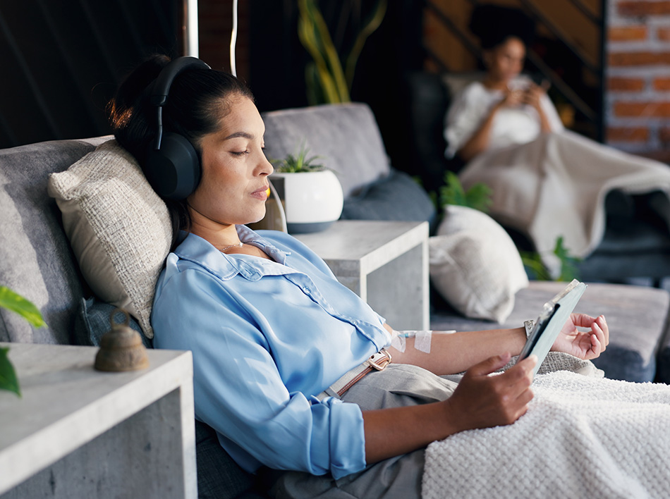 Woman reclining with headphones and tablet during IV therapy session, highlighting relaxation and wellness treatment.