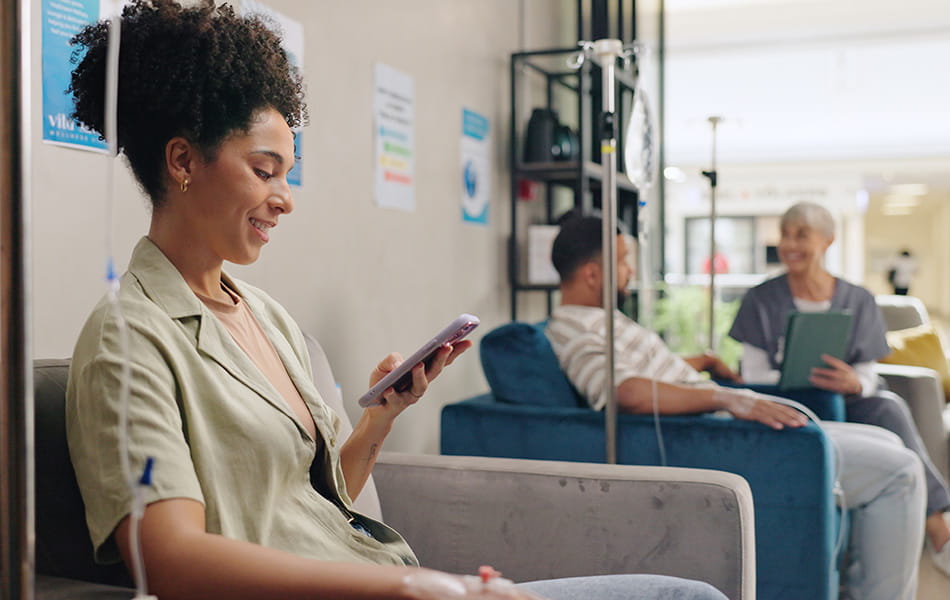 Woman using smartphone during IV infusion session, highlighting comfortable clinic treatment environment.