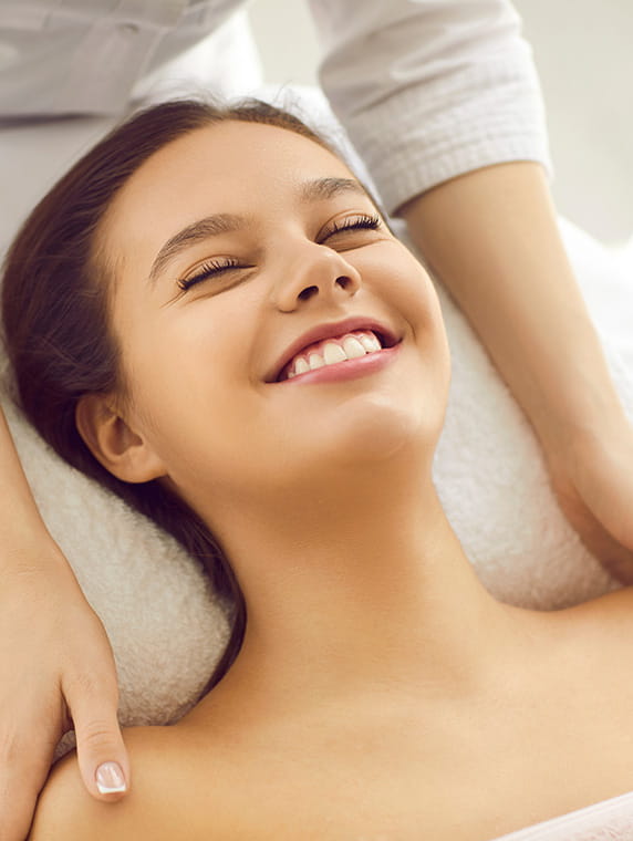 Smiling woman lying on spa bed during massage, highlighting relaxing wellness and skincare treatment.
