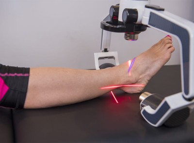 Laser device targeting ankle with red guide beams, highlighting noninvasive pain relief therapy.