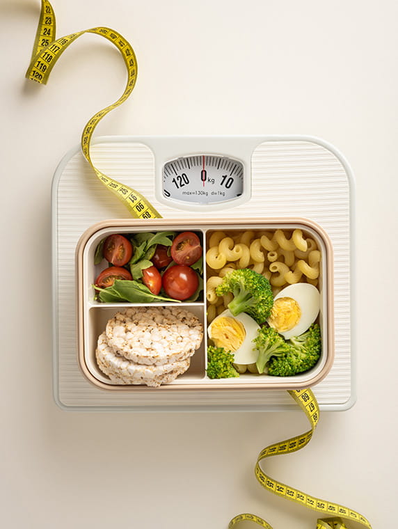 Healthy portioned meal on scale with measuring tape, highlighting balanced diet for weight management.