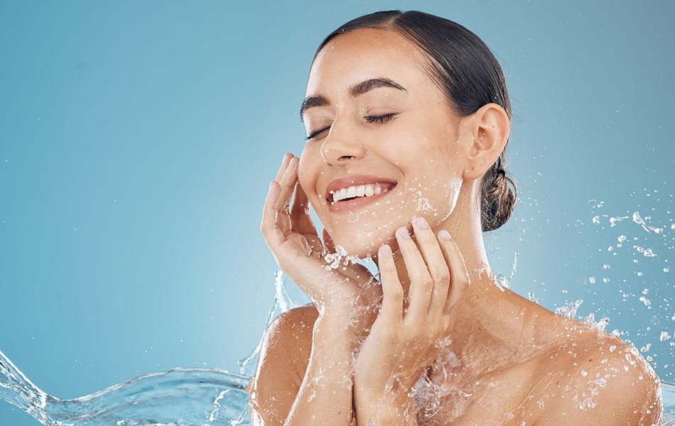 Smiling woman splashing water on face, highlighting refreshing cleansing skincare routine.