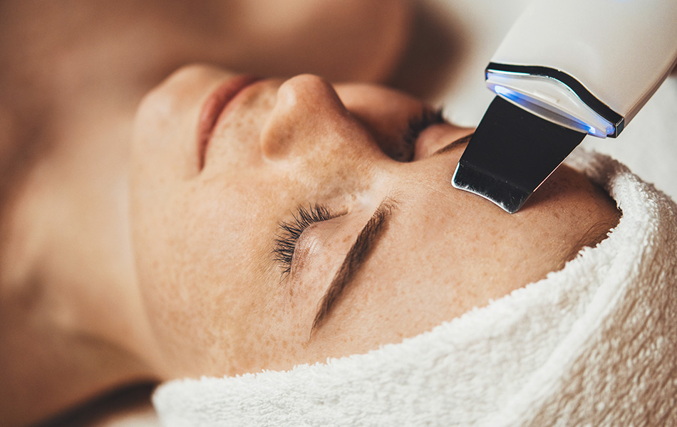 Woman receiving a face peel at a spa Esthetician using ultrasonic skin scrubber on woman’s forehead, highlighting professional facial treatment.