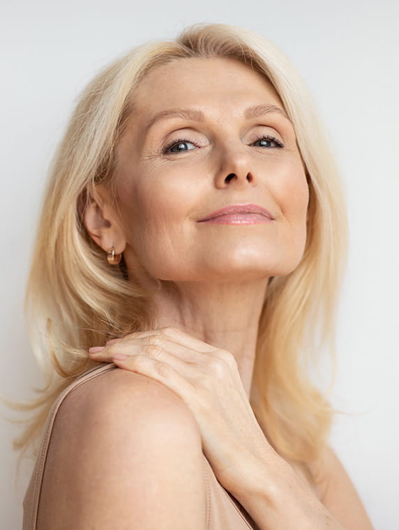 Confident older woman with smooth skin touching shoulder, highlighting anti-aging skincare results.