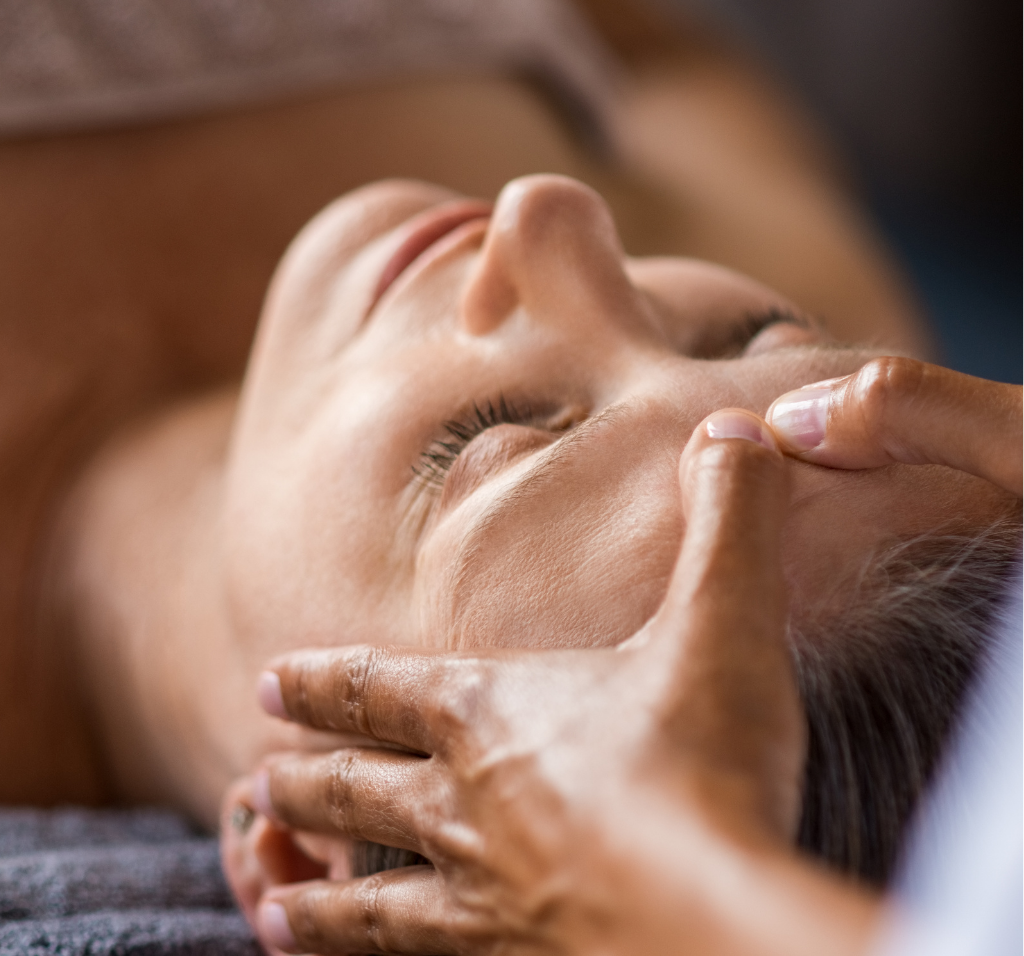 Untitled design (27) Woman lying on her back and receiving a facial massage